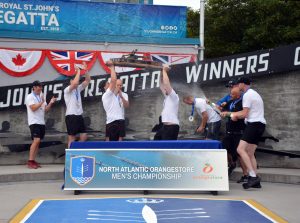 The winning men's championship team celebrate by hoisting the award above their head while a team mate sprays a bottle of champagne