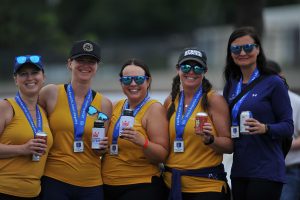 Female rowers in yellow gather to pose for the camera, they smile and cheers their beer